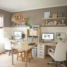 a home office with two computer desks and shelves on the wall above them,