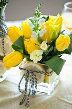 a vase filled with yellow flowers on top of a table next to two lemons