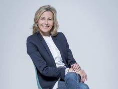 a woman sitting on top of a blue chair in front of a white wall with her legs crossed