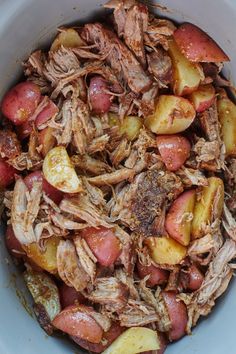 a bowl filled with meat and potatoes on top of a wooden table next to utensils