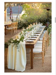 a long table with white linens and greenery is set for an outdoor dinner