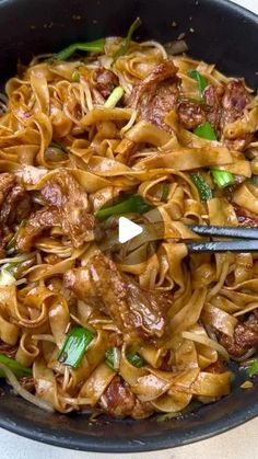 a skillet filled with noodles and meat on top of a white countertop next to a fork