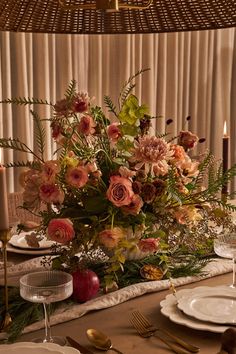 an arrangement of flowers and greenery is displayed on a dining room table with candles