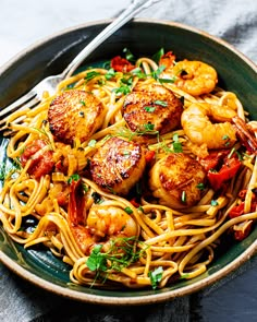 a bowl filled with pasta and shrimp on top of a table next to a fork