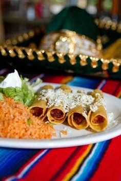 a white plate topped with three hot dogs next to rice and lettuce on a colorful table cloth