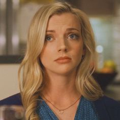 a woman with blonde hair and blue shirt looking at the camera while wearing a necklace