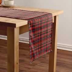 a red and black plaid table runner on top of a wooden table with a bowl of fruit