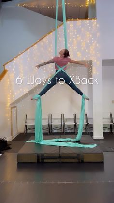 a woman is performing aerial acrobatic tricks on a beam in a room with string lights