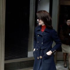 a woman in a blue coat and red turtle neck sweater is walking down the street