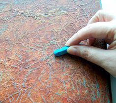 a hand holding a blue marker on top of a piece of paper that is covered in paint