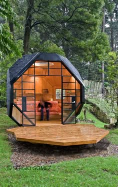 a small cabin in the middle of a forest with two people standing inside and looking at it