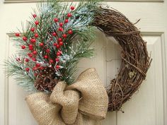 a wreath on the front door decorated with berries and pineconis is hung by a burlap bow