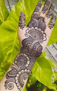 a hand with henna tattoos on it next to green plants and leaves in the background