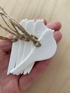 a hand holding four white ceramic angel wings with twine on each side and two strings attached to them