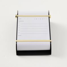 a notepad with a pen attached to it on a white surface next to a black and gold clipboard