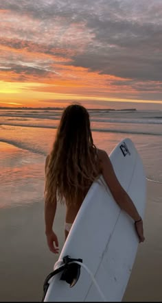 a woman holding a white surfboard on top of a sandy beach near the ocean