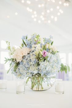 a vase filled with blue and white flowers on top of a table next to two candles