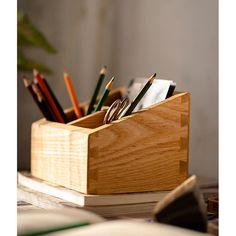 a wooden box filled with pens and pencils on top of a desk next to a plant