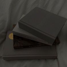 three books sitting on top of each other on a white bed sheet in front of an alarm clock