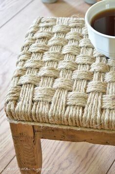 a cup of coffee sitting on top of a wooden table next to a woven seat