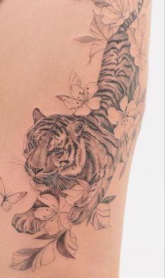 a tiger and butterfly tattoo on the back of a woman's thigh, with flowers around it