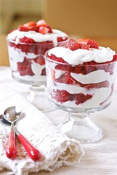 two desserts with strawberries and whipped cream in them on a white tablecloth