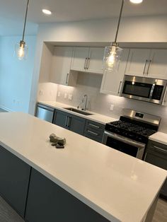 an empty kitchen with stainless steel appliances and white counter tops, along with gray cabinets