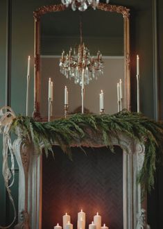 a mantel with candles and greenery on it in front of a chandelier