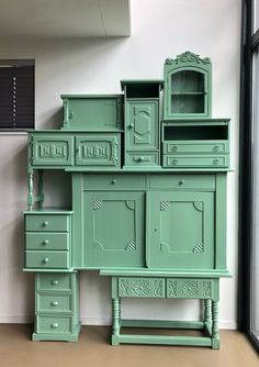 a green dresser sitting in front of a window next to a tall cabinet with drawers