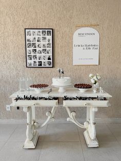 two white tables topped with cakes and desserts in front of a poster on the wall