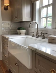 a white kitchen sink sitting under a window next to a counter top with a potted plant on it