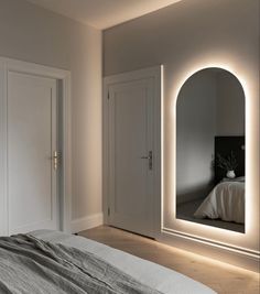 a white bed sitting under a large mirror next to a wall mounted light above it