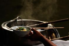 a person holding a bowl with food in it on top of a stove burner