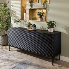 a black dresser with plants on it in front of a mirror and potted plants