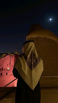 a woman standing in front of a tall building at night with the moon behind her