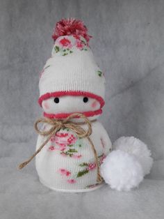 a small stuffed snowman is wearing a white hat and pink flowered sweater with a pom - pom