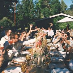 a group of people sitting around a wooden table with plates and glasses on top of it