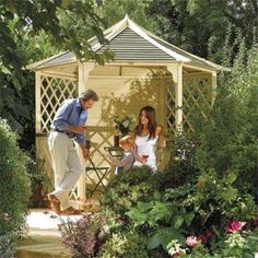 an older man and young woman standing in front of a gazebo surrounded by flowers