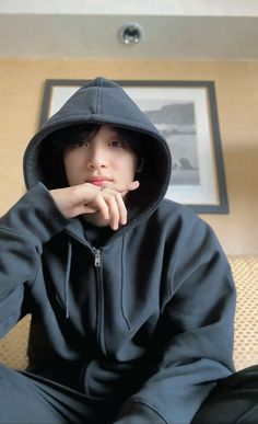 a young man sitting on top of a couch wearing a black hoodie and holding his hand under his chin