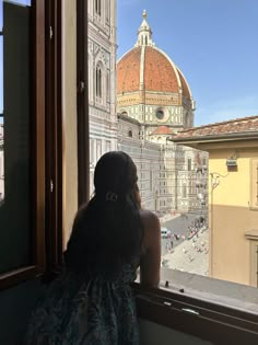 a woman looking out the window at an old building with a dome in the background