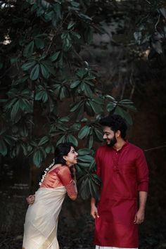 a man and woman standing next to each other near a tree with leaves on it