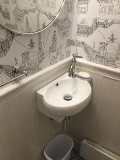 a white sink sitting under a mirror in a bathroom next to a wallpapered wall