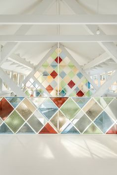 an artisticly designed glass window in a building with white walls and beams, along with multicolored tiles on the wall