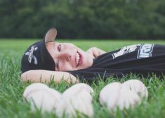 a young boy laying in the grass with baseballs