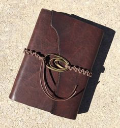 a brown leather journal with a chain on the front and bottom cover, sitting on a concrete surface