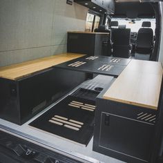 the interior of an rv with black seats and wooden tables on each side, along with wood flooring