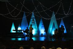 a group of people standing on top of a stage next to christmas trees in the dark