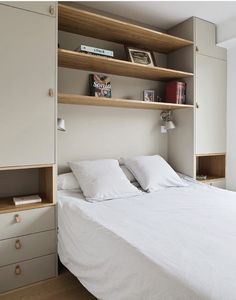 a white bed sitting in a bedroom next to a wooden shelf filled with books and magazines