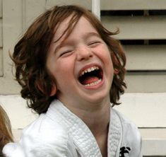 a young boy laughing while wearing a karate outfit