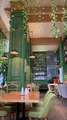 the interior of a restaurant with green painted walls and wooden tables surrounded by chairs, hanging plants and potted plants